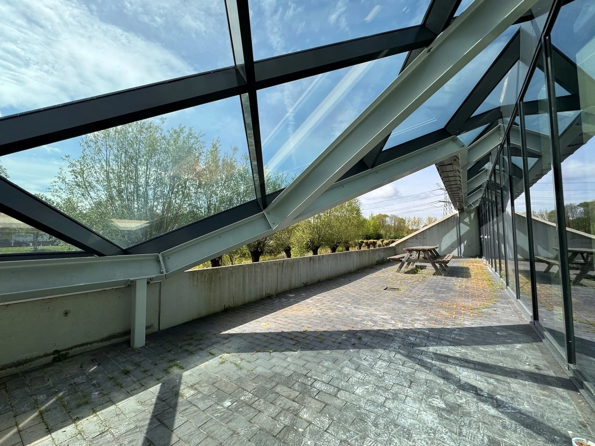 Terras met picknicktafels naast het moderne glazen gebouw Mart Stamhof, onder een schuin glazen dak.